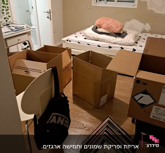חדר עם קופסאות קרטון פתוחות וערימת תקליטים